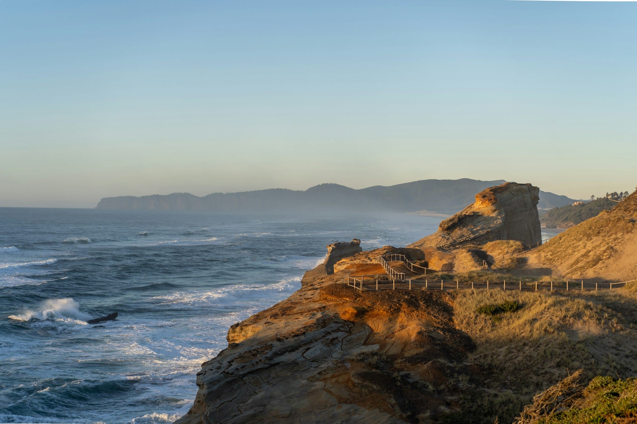Golden evening light on the sandstone cliffs of Cape Kiwanda, with waves rolling in toward Pacific City, Oregon.